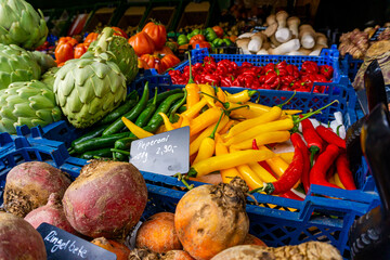 Closeup of yellow, green and red peppers, artichokes, rutabagas and other vegetables at a street market stall. Colourful background