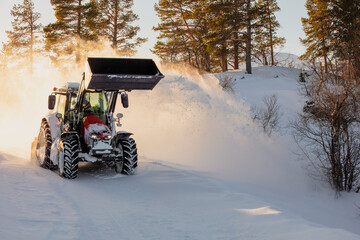 Snow plow tractor cleaning snow with a large bucket on countryside road. Sun backlight. Winter...