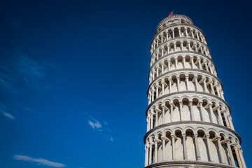 The iconic Leaning Tower of Pisa with its arches against a clear blue sky. Landscape view.