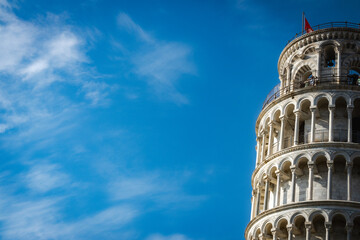 The iconic Leaning Tower of Pisa with its arches against a clear blue sky. Landscape view.