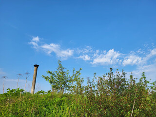 Against the background of a blue sky with feathery clouds, a thin chimney protrudes from behind...