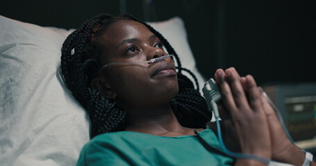 Hospitalized African woman with nasal oxygen tube, praying earnestly.