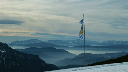 Bavarian flag stands tall in a snow-covered mountainous region with a breathtaking horizon.