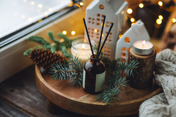 Natural Christmas essential oil, home aroma diffuser. Burning candles, branches of fir tree. Cinnamon, vanilla smell. Aromatherapy, cozy atmosphere, holiday festive mood. Close up macro, wooden table
