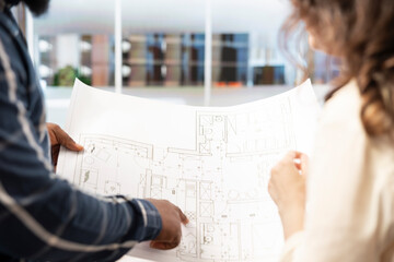 Real estate agent explaining office space layout to client using blueprints and architectural...