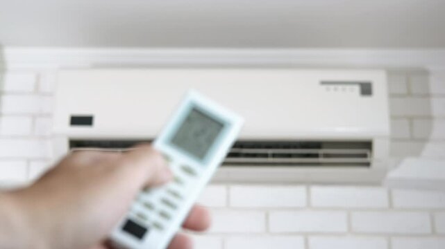Sets selects temperature of air cooling. A view of man hold the remote controller and select the temperature on the air conditioner in the apartment.