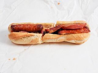Traditional Irish breakfast roll with cooked sausages, bacon or rashers and black and white pudding in a round bread on light color paper. Popular meal with high calorie count.