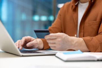 Asian businessman using credit card and laptop for online payment. Image captures essence of modern finance, technology, e-commerce, and business transactions with focus on convenience.