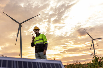 Professional Man Maintenance engineers working in wind turbine farm at sunset. Engineer Man standing among Wind Energy Turbine.