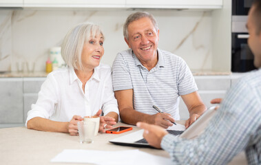 Obraz premium Couple of elderly man and woman discussing deal with male salesman in kitchen home