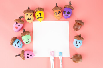 Colorful acorns with facial expressions around blank white square, pink background, painted acorns, autumn craft, educational art, kids activity, nature inspired design,