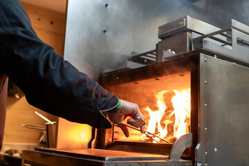 Chef Adjusting Fire in a Grill Oven at a Restaurant Kitchen