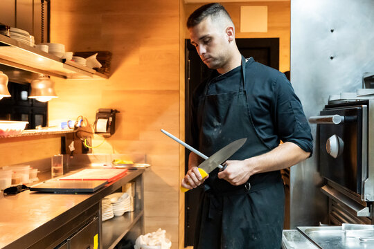 Professional chef sharpening knife in busy kitchen