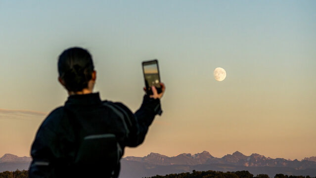 Anonymous person capturing the Moonset in Estavayer le Lac, Switzerland