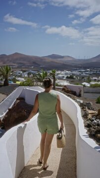 Woman walking on a pathway in lagomar lanzarote with scenic view of distant mountains and wind turbines under clear blue sky
