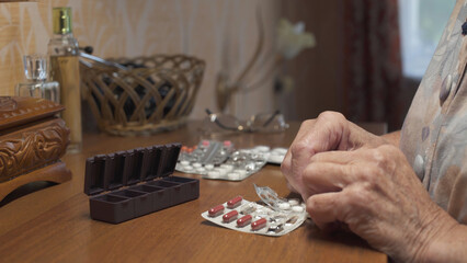Old woman putting pills into pill box medicine container. Hands close-up.