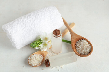 Bottles with rice water, grains, flower and clean towel on light background