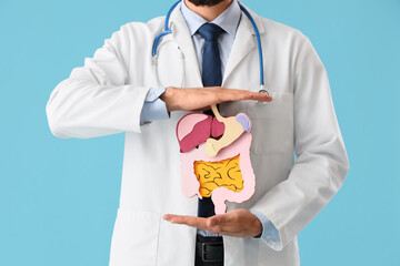 Male neurologist with model of digestive system on blue background, closeup