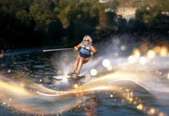 Fototapeta premium A woman in a life vest water skis on a lake. The sun creates a shimmering glow on the water.