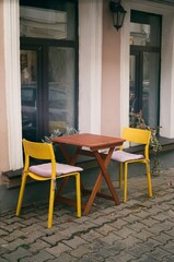 Film photo of wooden brown coffee table with two yellow chairs standing near windows of coffee shop