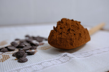 Spoonful of cocoa powder with chocolate chips on tablecloth