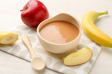 Delicious baby food in bowl and ingredients on white wooden table