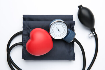 Blood pressure measuring device and red decorative heart on light background, top view