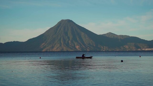 Man in his boat, preparing to fish in the calm dawn of Lake Atitlan. The soft light of the newly emerging sun illuminates the water as the volcanoes rise majestically on the horizon.