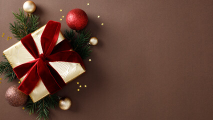 Christmas elegant holiday flat lay with gold-wrapped gifts, red ribbons, pine branches, and festive baubles on a dark brown background