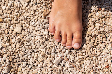 Close up of child is foot on pebble beach under the sun, highlighting natural textures and warmth...
