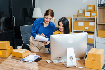 Two young female entrepreneurs run small online clothing store. In a warehouse filled with parcel boxes, they work on laptops, designing clothing and preparing sales brochures and business proposals.