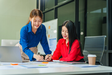 Two young female business consultants work on startup, collaborating on mobile app development social media strategies. whiteboards, documents, they aim to build a successful e-commerce business.