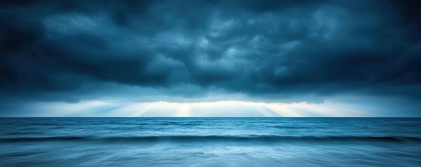 Obraz premium Dark stormy clouds above a calm ocean with gentle waves and distant light.