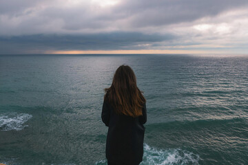 Fototapeta premium Mujer joven que se siente sola y triste o pensativa o esperando. mirando el mar en un día sombrío , Young woman feeling alone and sad or thoughtful or waiting. looking at the sea on a gloomy day