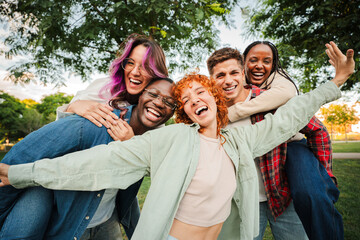 Group of joyful young friends having fun outdoors, embracing and laughing together in a park. Energetic, carefree and multiracial people enjoying a lively and playful moment of friendship