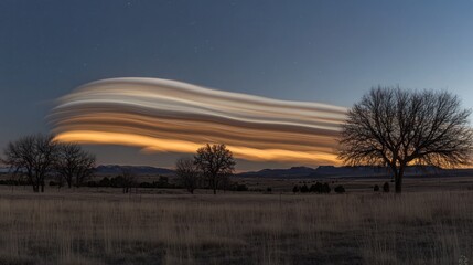 A long exposure photograph of a lenticular cloud formation over a field with trees at dusk.