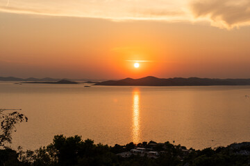 Fototapeta premium Beautiful sunset over tranquil sea with warm golden tones reflecting off the water and distant islands on the horizon. Peaceful landscapes. High quality photo
