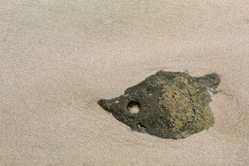 Large black coral rocks with a rough texture on the beach.