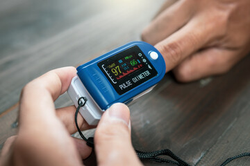 Pulse oximeter on male fingertip on dark wooden table background, medical equipment, portable oximeter