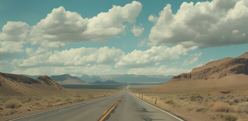 A long, open road stretches through a desert landscape under a blue sky filled with fluffy clouds, leading to distant mountains.