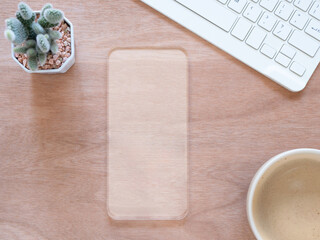 Transparent mobile phone model empty display mock-up with coffee cup and cactus, keyboard on wooden background. Top view composition. Concept online shopping, blog, logo, social media, and product.