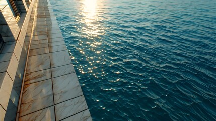 Fototapeta premium A tiled edge of a dock or deck meets the ocean's surface, reflecting sunlight on the rippling water.