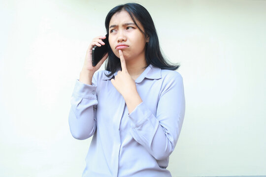 anxious worried asian young woman talking on mobile phone and thouch her chin with forefinger, female dressed in formal suit looking away, isolated over white background