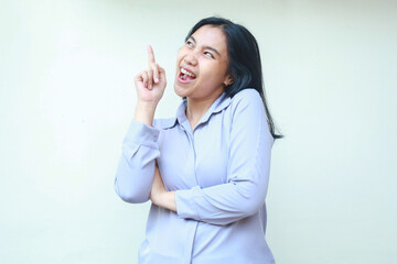 excited asian young business woman pointing up with arm folded and looking above dressed in formal suit, female isolated on white background