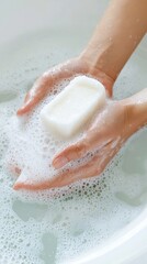 Hands holding a bar of soap in a bubble-filled bathwater.