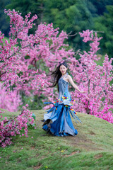 A joyful woman dances in a flowing denim dress surrounded by vibrant pink blossoms, celebrating nature and springtime outdoors.