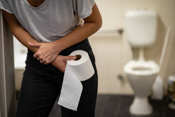Young female hunched over and holding stomach, perhaps needing to use the bathroom or toilet,...