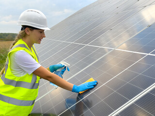 Washing solar panels. A young girl washes a solar power plant. A girl in a eflective vest cleans solar panels