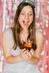 A girl at the birthday party blowing candles and making a wish holding a cake and three candles