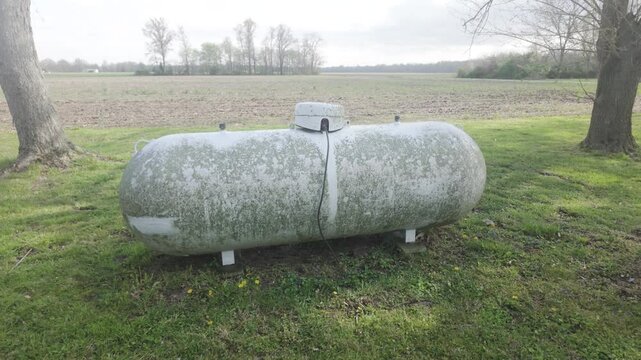 zoom in shot of a propane tank sitting on green grass with a field landscape background on a sunny but overcast day